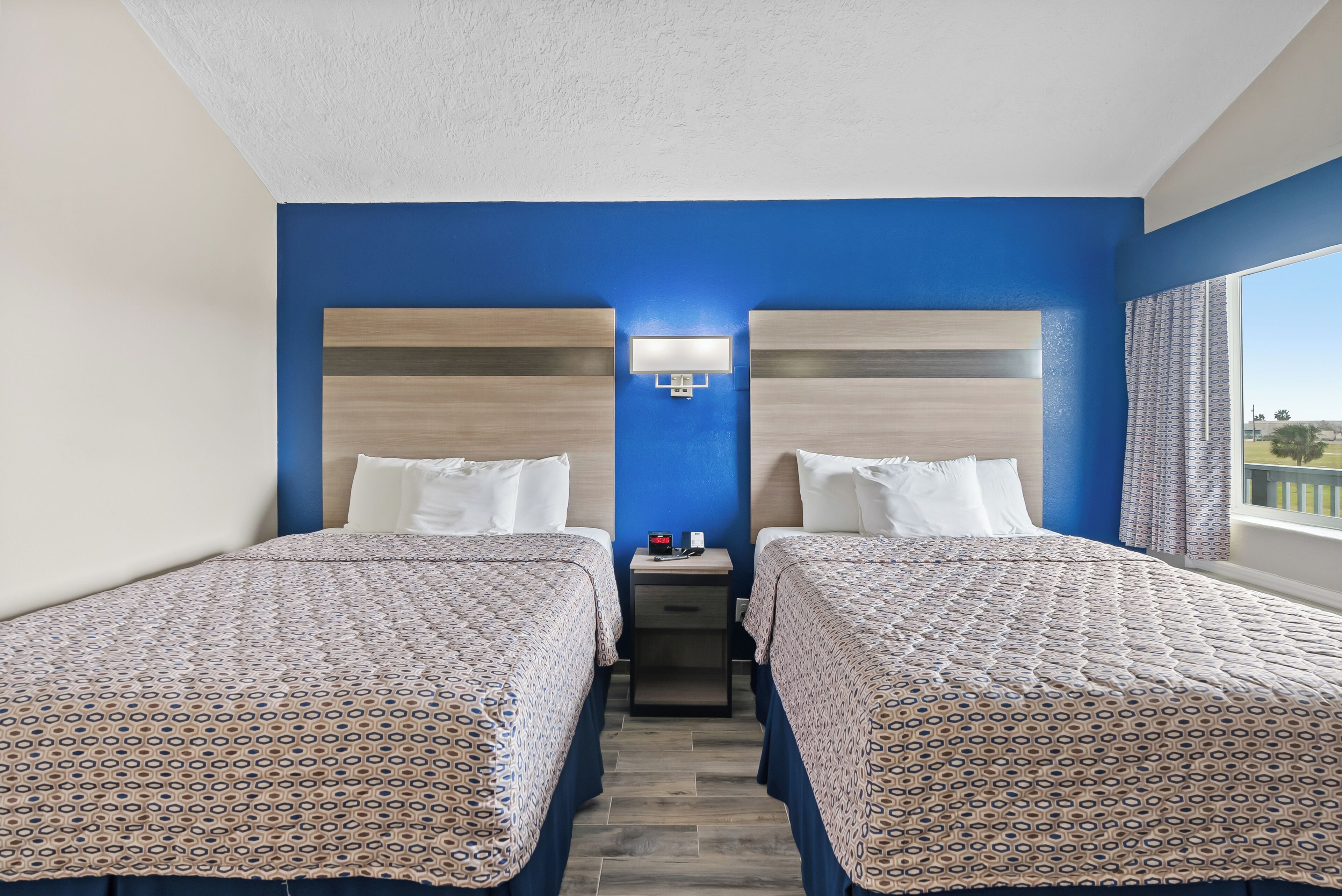 A hotel room with two beds, a nightstand, and a window with curtains.