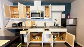 Een kleine keuken met witte kastjes, een magnetron, een broodrooster en een koelkast.