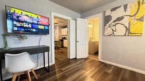 Een moderne woonkamer met een flatscreen televisie aan de muur, een bureau met een stoel, en een groot abstract schilderij.