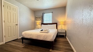 Een slaapkamer met een bed, twee nachtkastjes met lampen, een deur en een raam met jaloezieën.