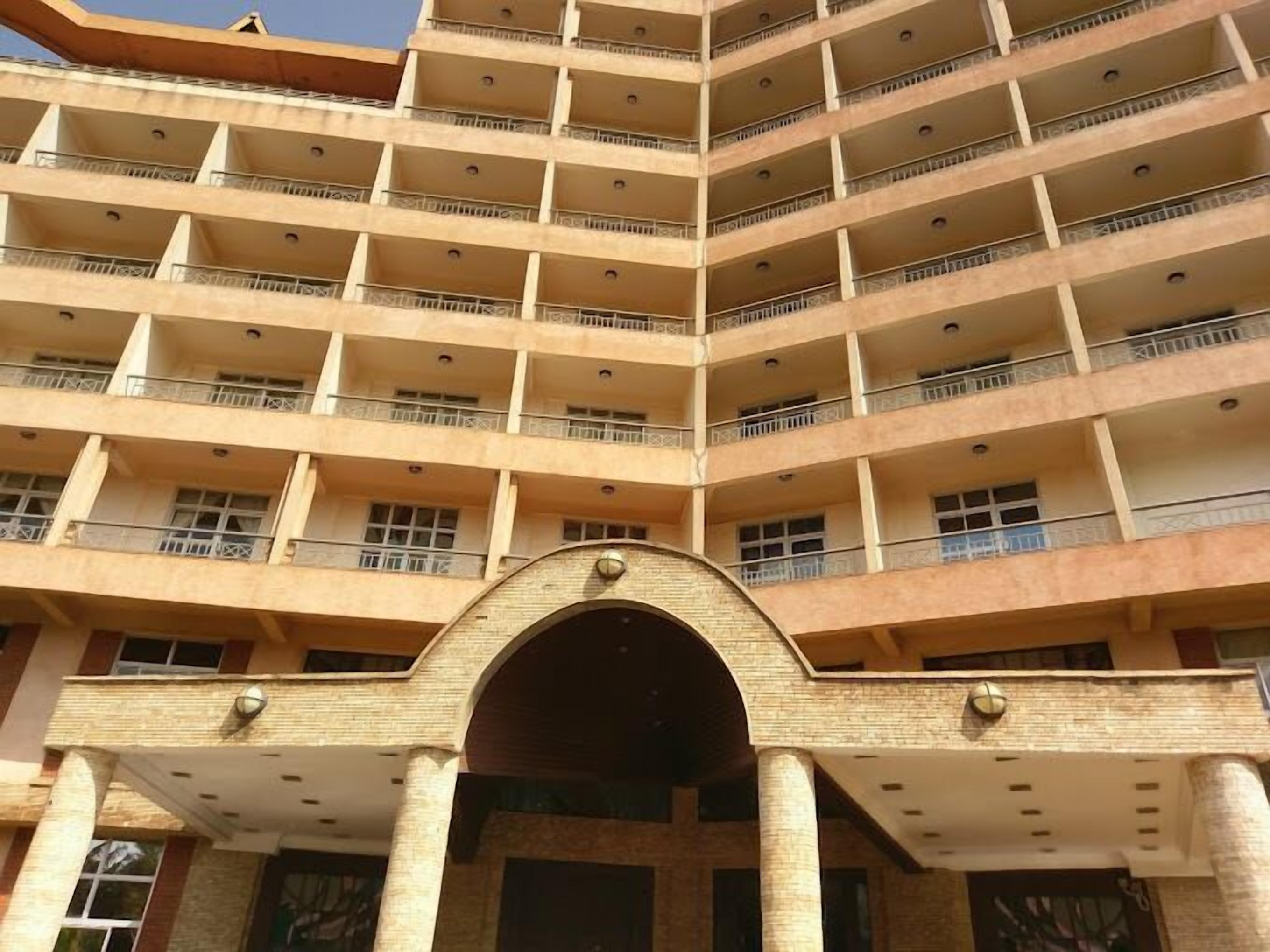 A multi-story building with a central entrance, balconies on each floor, and a brick facade.