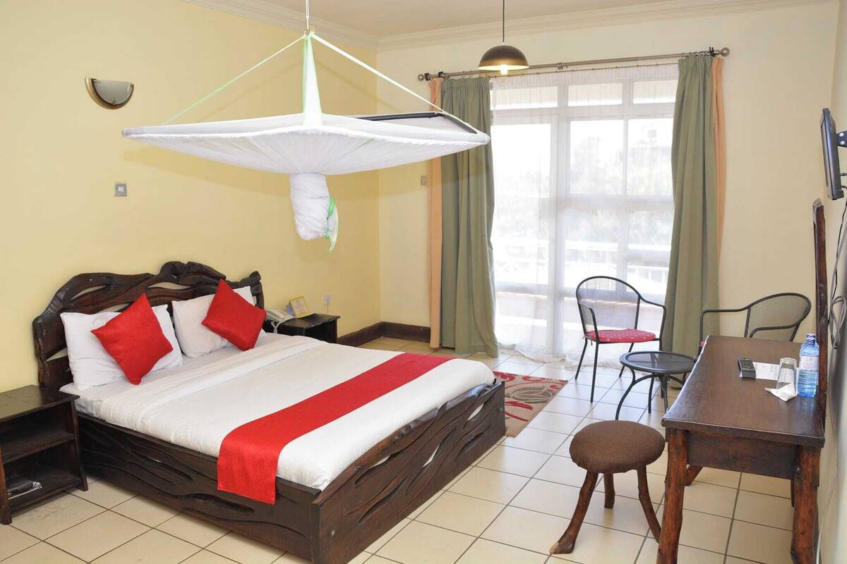 A hotel room with a bed, bedside table, chair, desk, and a window with curtains.