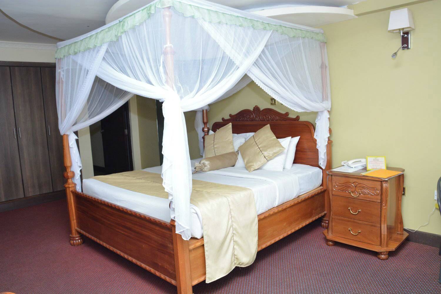 A four-poster canopy bed with a wooden headboard, a bedside table with a telephone, and a wall-mounted lamp.