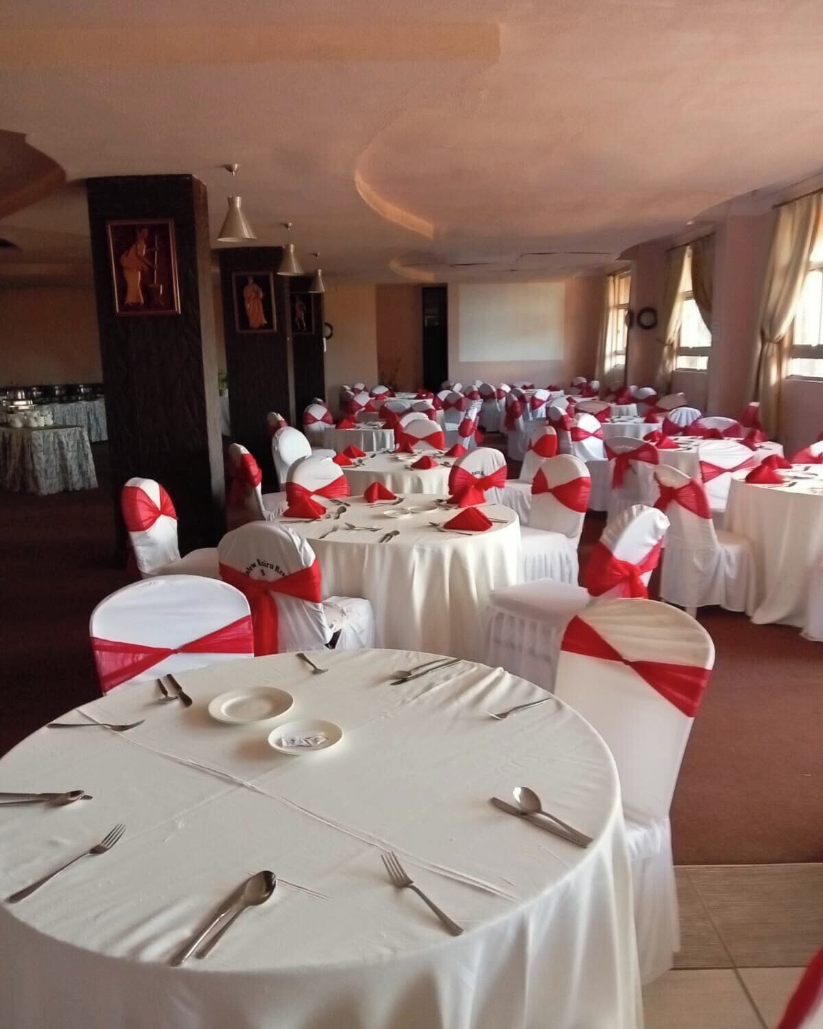 A banquet hall with round tables set for a formal event, featuring white tablecloths and red sashes on chairs.