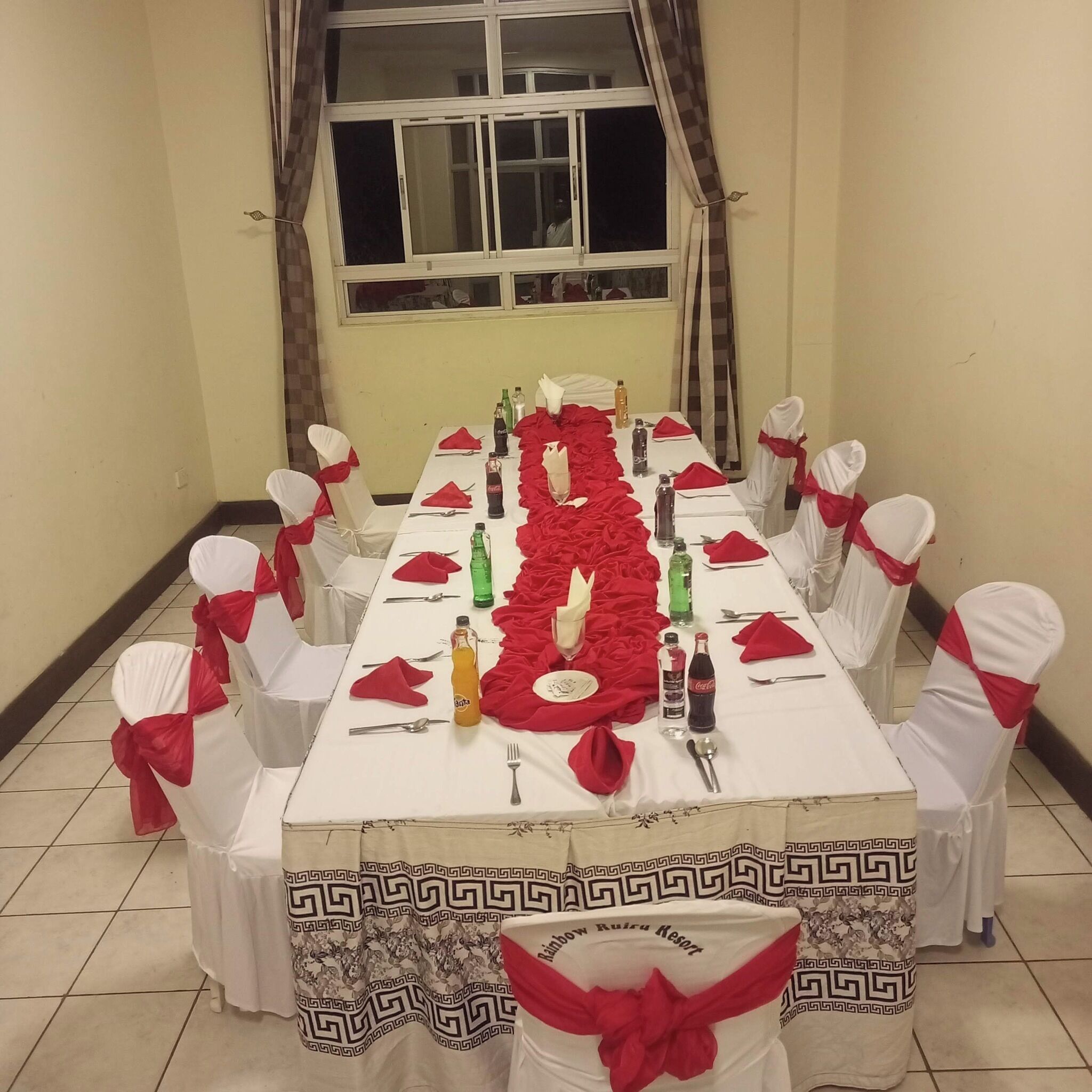 Une table à manger dressée pour un repas, avec des chaises, une fenêtre et des rideaux.