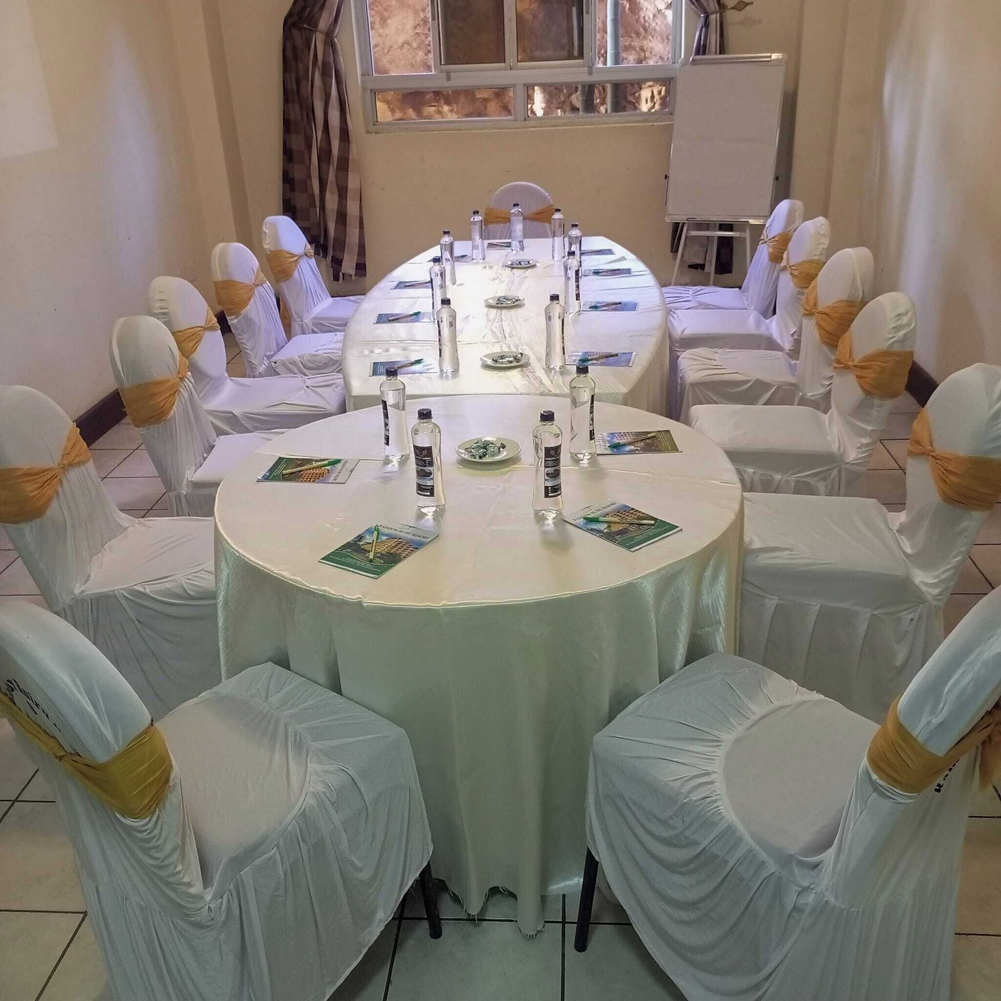 A conference room with a round table, white chairs with yellow sashes, and a white tablecloth.