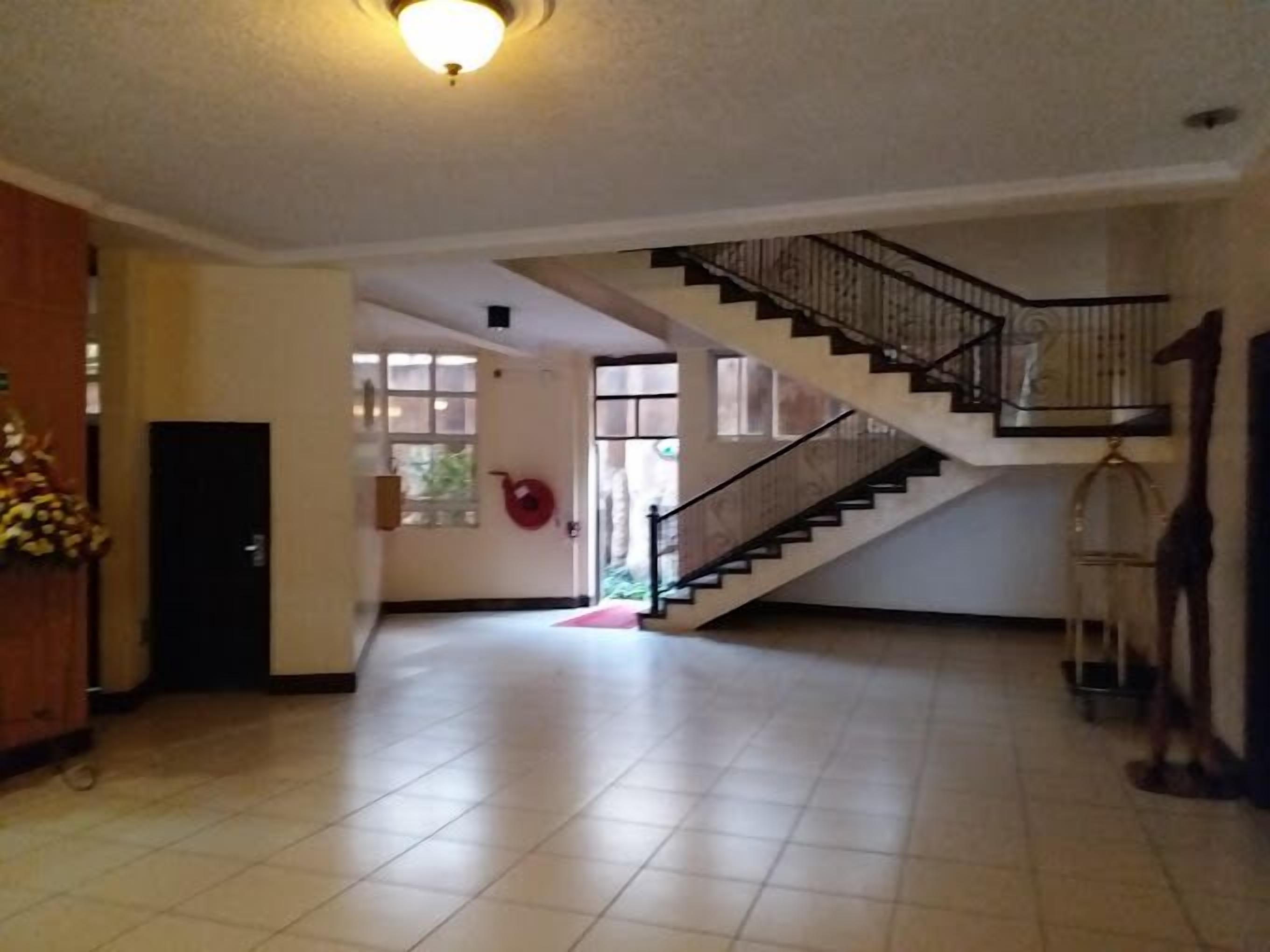 A spacious interior with a staircase leading to an upper floor, tiled floors, and a door with a red mat.