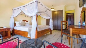 A room with a four-poster bed, a wooden desk, a chair, and a television on the wall.