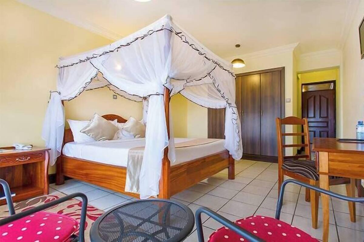 A room with a four-poster bed, a wooden desk, a chair, and a television on the wall.