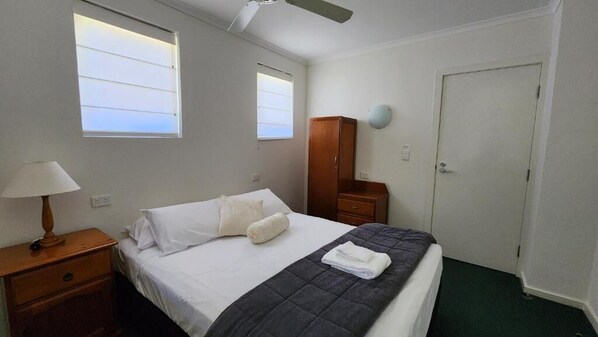 Una habitación de hotel con cama, mesita de noche con lámpara, armario y puerta.