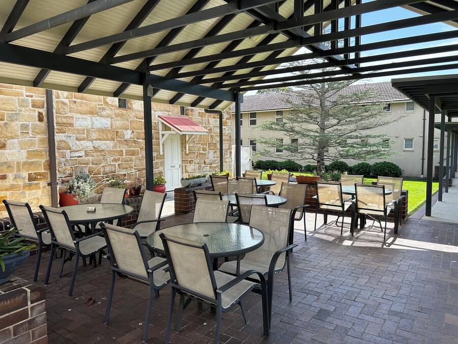 An outdoor patio area with stone walls, multiple tables and chairs, and potted plants.