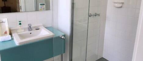 A modern bathroom with a glass shower enclosure, a sink with a teal countertop, and a mirror above the sink.