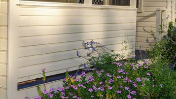 A house with a porch, a covered front entrance, and a garden with purple flowers.