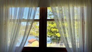 Una ventana con cortinas blancas traslúcidas, vista de un edificio y árboles.