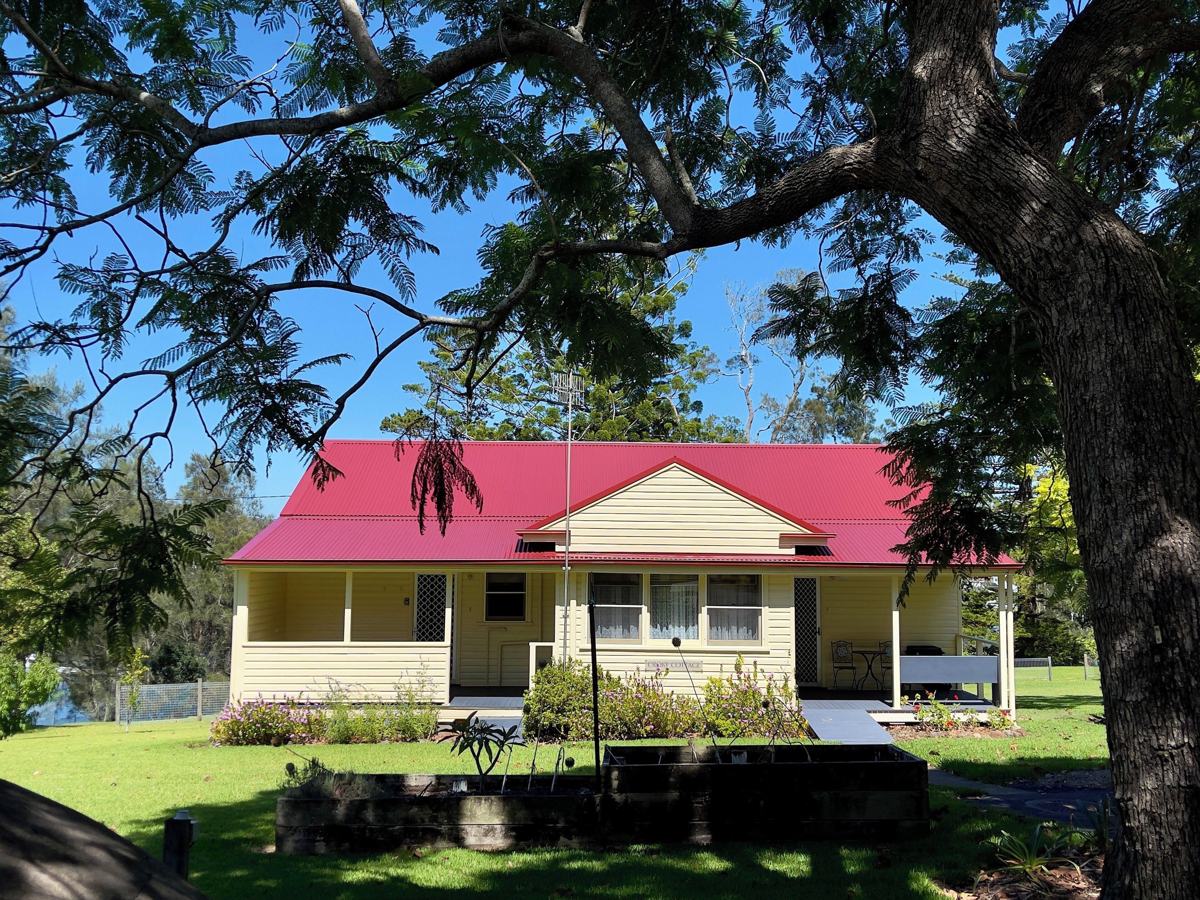 Una casa amarilla con techo rojo, rodeada de árboles y un césped bien cuidado.