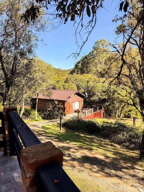 A rustic cabin with a red roof, surrounded by lush greenery and hills. - Montanhas do campestre hospedagem (Urubici)