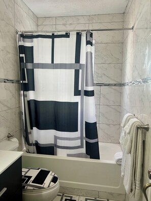 Een badkamer met douchegordijn, toilet en bad.