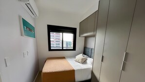 A bedroom with a bed, a window, an air conditioner, and a wardrobe.