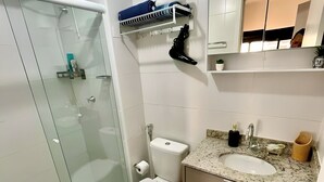 A modern bathroom with a glass shower enclosure, a toilet, a sink with a marble countertop, and a mirror above the sink.