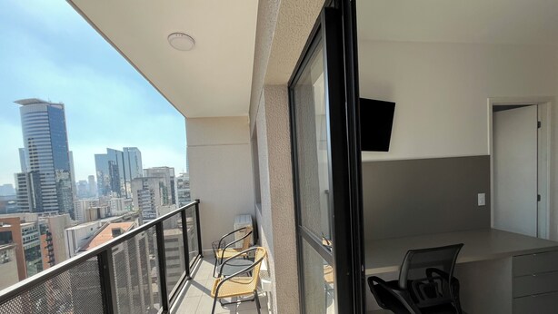 A balcony with a city view, a chair, a desk, and a TV mounted on the wall.
