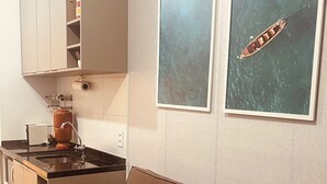 A modern kitchen with a built-in oven, a coffee machine, and a sink. There is a brown sofa with cushions and two framed pictures on the wall.