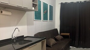 A compact kitchen with a black countertop, a built-in oven, and a sink. A brown sofa is placed against the wall, and there are three framed pictures above it.