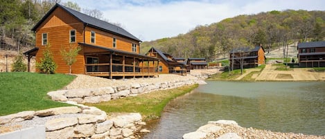 A wooden lodge with a stone-lined water feature and a view of the surrounding hills.