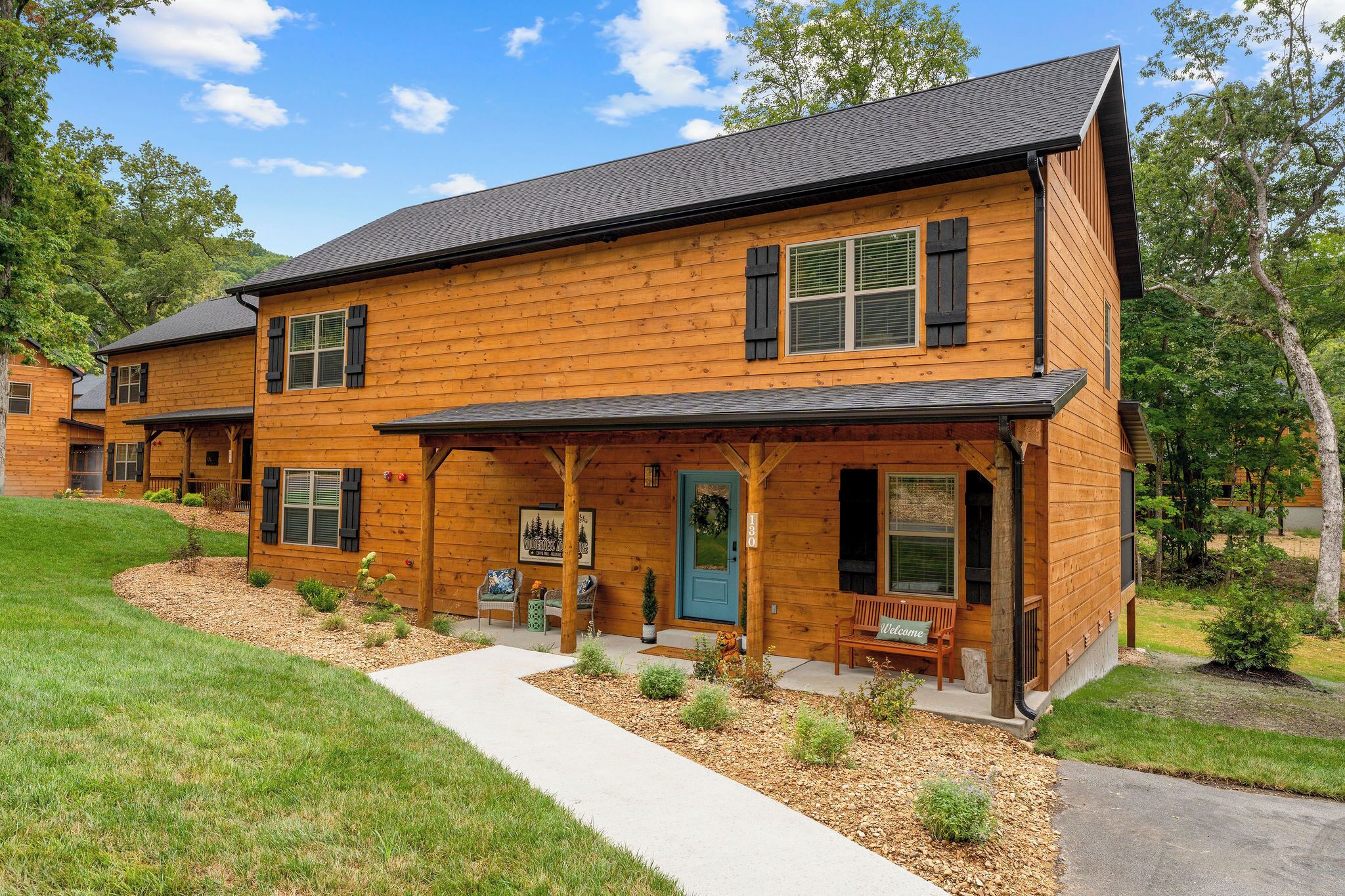 A two-story log cabin with a porch, a front door, and a small garden area.