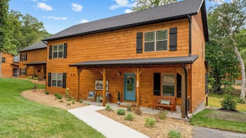 A two-story log cabin with a porch, a front door, and a small garden area.