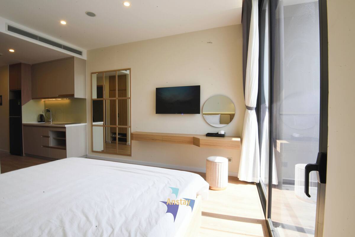 Habitación de hotel con cama, televisión, espejo, una mesita y vistas al exterior.