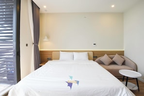 A hotel room with a large bed, a small sofa, a round table, and a window with blinds. - ICON40 Ha Long  Managed by Anstay (Bai Chay)