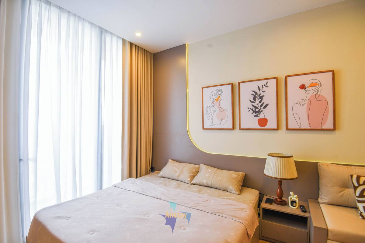 Una habitación de hotel con una cama grande, una mesita de noche con lámpara y tres cuadros enmarcados en la pared.