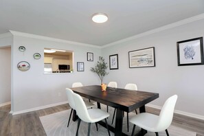 Un comedor con mesa de madera oscura, sillas blancas y un florero con planta.
