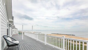 A wooden deck with a white railing, a black chair, and a view of the beach and ocean.