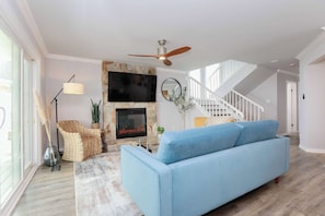 Una sala de estar con un sofá azul, una chimenea, un ventilador de techo y una escalera.