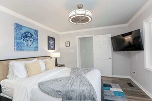 A bedroom with a bed, a ceiling fan, a TV mounted on the wall, and a door.