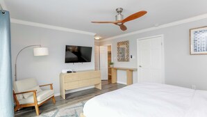 A hotel room with a bed, a desk, a chair, a TV, and a ceiling fan.