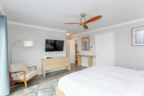 A hotel room with a bed, a desk, a chair, a TV, and a ceiling fan.