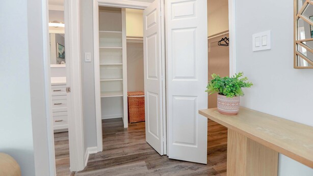 A hallway with a wooden floor, white walls, and a white door leading to a closet.