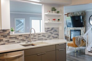 A modern kitchen with a large window, a built-in sink, and a flat-screen TV mounted above the fireplace.