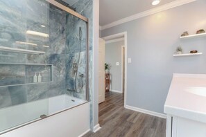 A modern bathroom with a glass-enclosed shower, a white sink, and wooden flooring.