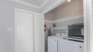 A laundry room with a front-loading washer and dryer, a fire extinguisher, and a ceiling-mounted iron.