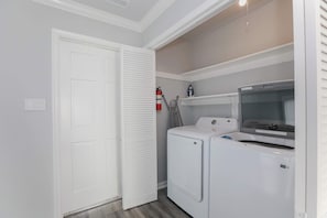 Ein Waschraum mit einer Waschmaschine und einem Trockner, einem Feuerlöscher und einem an der Decke befestigten Bügeleisen.