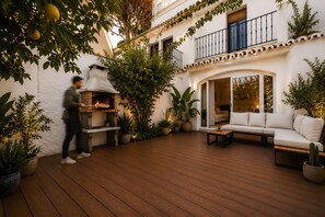 A courtyard with a wood-floored patio, outdoor seating, a brick oven, and potted plants. - Los Arcos | Charming Patio Pool Townhouse (Marbella)