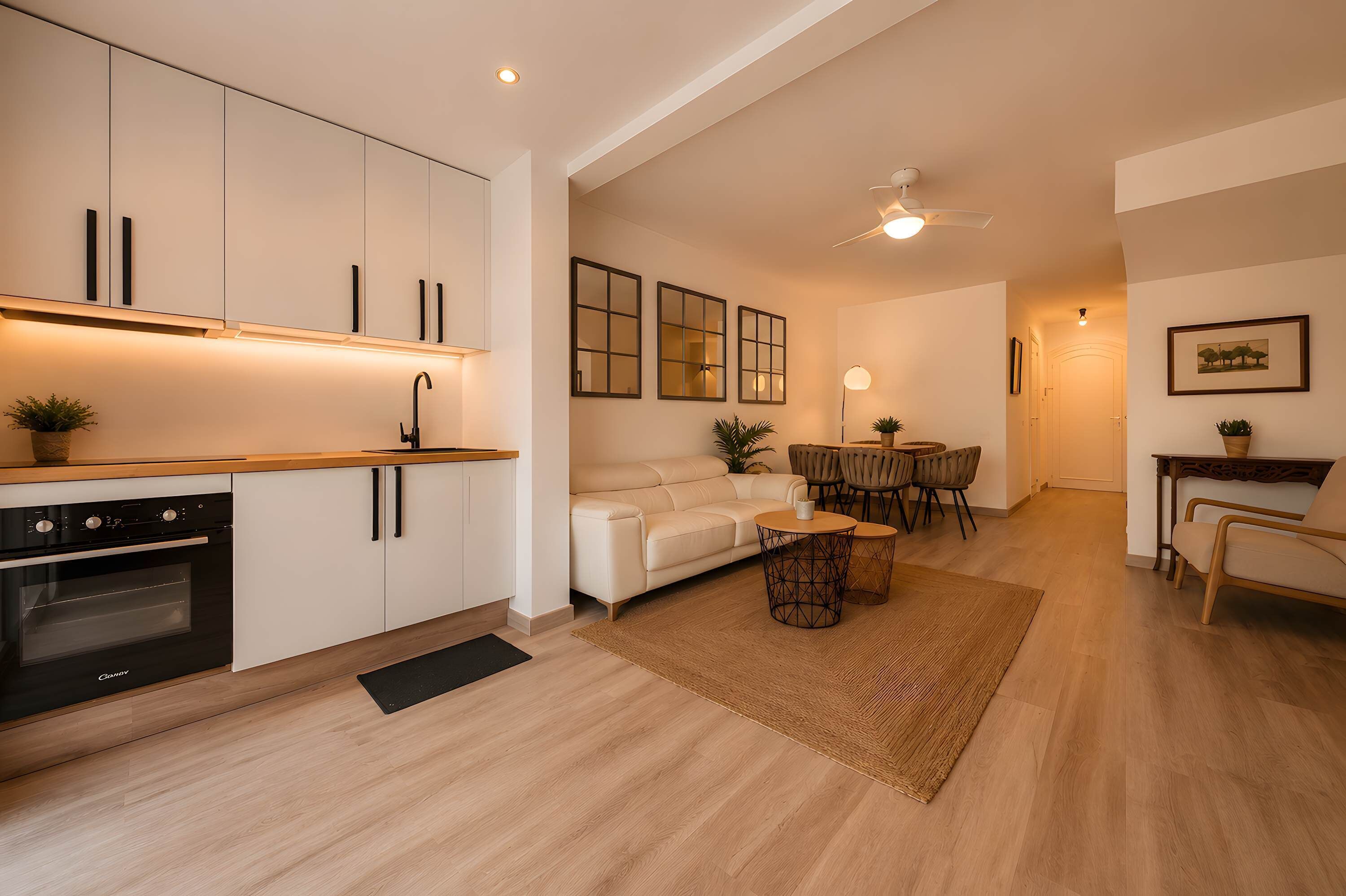 A modern kitchen with white cabinets, a black oven, and a dining area with a white sofa and wooden table.
