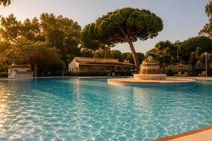 A swimming pool with a fountain, surrounded by trees and a building with a tiled roof.