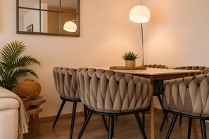 Een eetruimte met een ronde tafel, gestoffeerde stoelen, een vloerlamp, een potplant en een spiegel aan de muur.