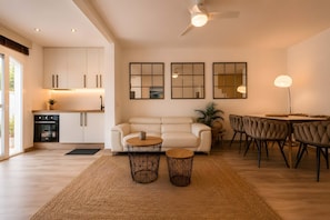 A modern living room with a sofa, two coffee tables, a dining table with chairs, and a kitchen in the background. - Los Arcos | Charming Patio Pool Townhouse (Marbella)