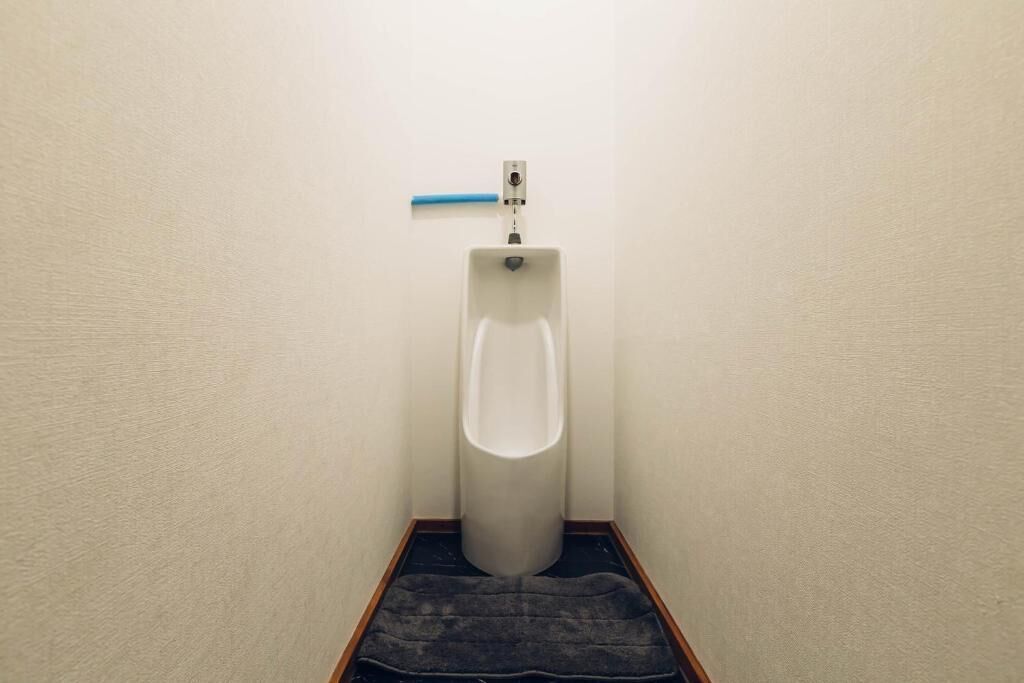 A urinal in a corner with a blue towel on the floor.
