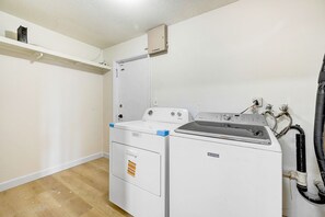 A laundry room with a washing machine and dryer, a shelf above the dryer, and a water heater on the wall. - Anchor14 | Coastal Getaway on Merritt Island (Merritt Island)